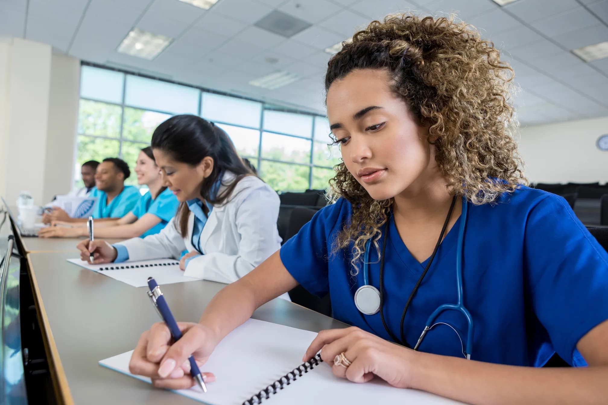 Nursing student in scrubs taking notes in class